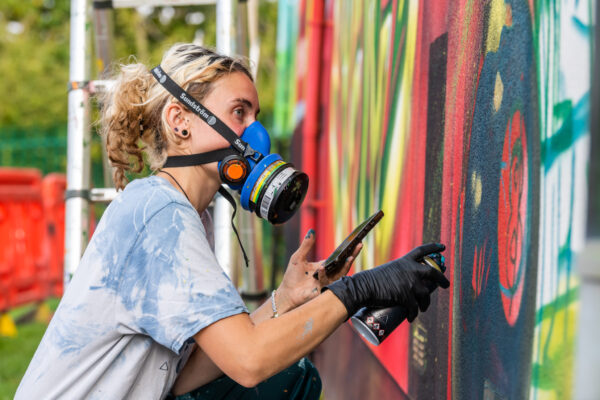 Artist Peachzz, wearing a pray paint mask as she sprays onto MAPA's community centre's wall.