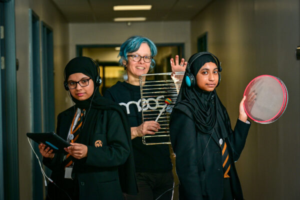 Two girls and a woman hold instruments in a school hall way.