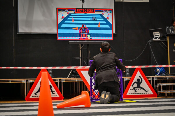 A young boy in school uniform with his back to the camera plays a computer game surrounded by traffic cones and signs