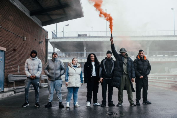 Group of young adults outside, one in the middle holding an orange flare