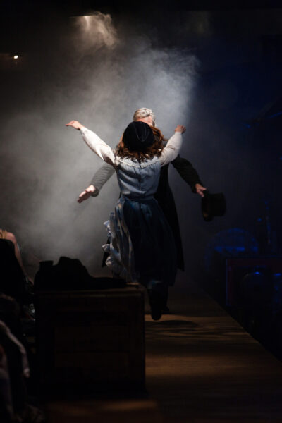 Two people run towards each other in a smoke filled room, both wearing Victorian era clothes