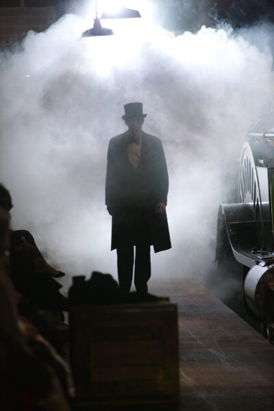 A tall, dark figure emerges from the smoke - dressed in Victorian era clothes.