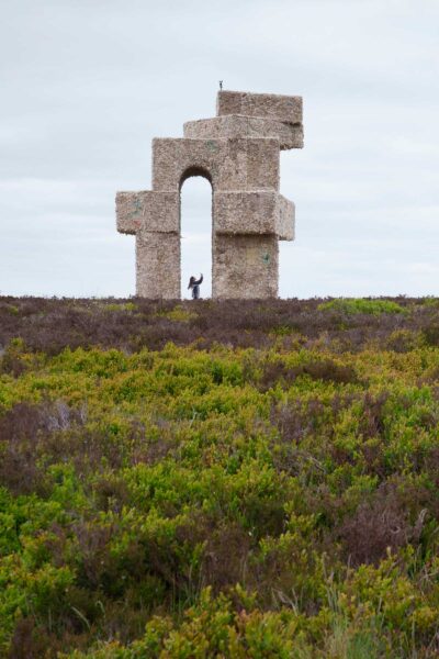 The artwork Tower by Steve Messam, in the landscape of Penistone Hill. The large sculpture is covered in sheep fleece, creating the shape of an arch with angular corners, set against a cloudy sky and the natural landscape.