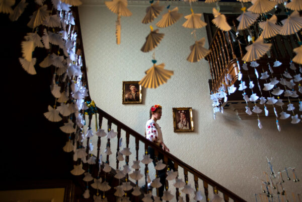 A girl wearing traditional Ukrainian dress walks down a set of stairs. There are paper sculptures hanging from the ceiling.