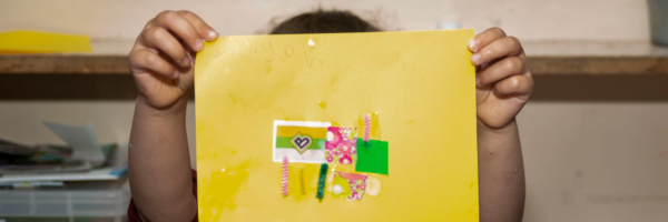 Handmade Bradford logo on a yellow piece of card, being held by a young person in front of the word 'creative'