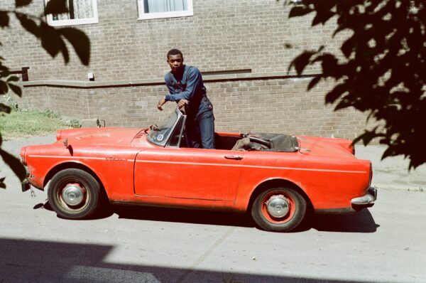 A man stands in a red convertible car.