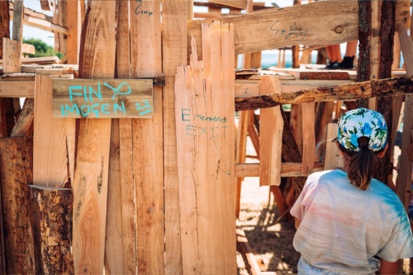 A young girl in a baseball cap enters a wooden structure.