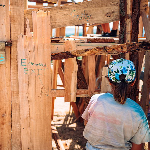 A young girl in a baseball cap enters a wooden structure.