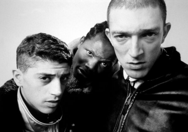 Three young men wearing jackets grouped together looking into the camera. The picture is black and white.