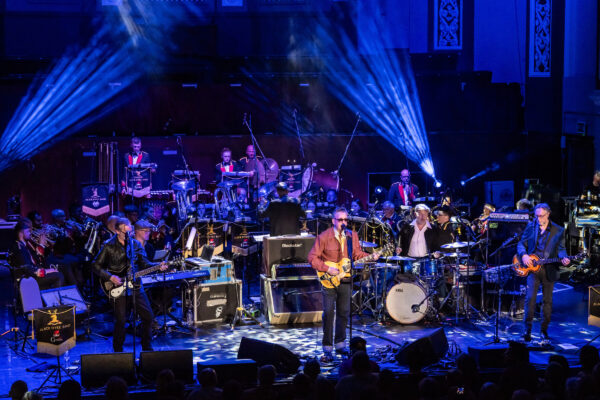 A man performs with a guitar in front of a full symphony orchestra