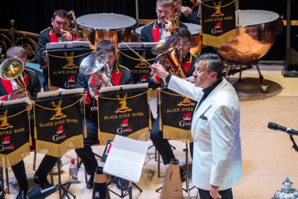 A conductor in a white suit jacket leads a brass band