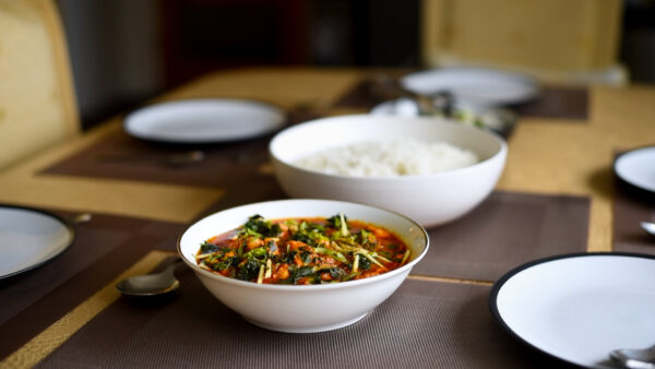 An image of a delicious looking chicken curry in a bowl, with rice in the background.