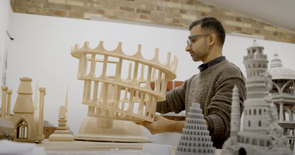 Saad holding a peice of the sculpture Tower Of Now, a wooden design