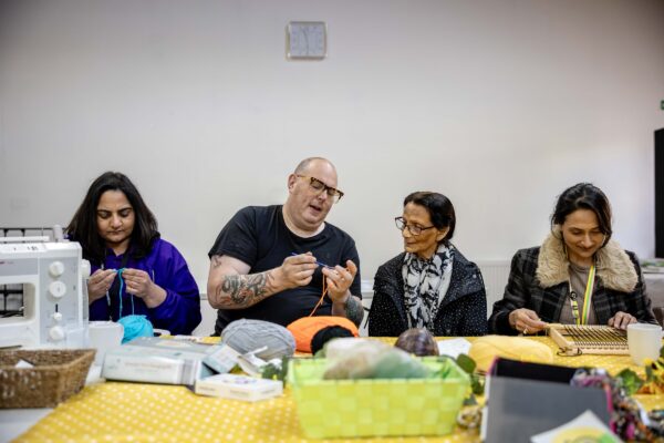 three ladies and a man sat chatting and knitting around a table