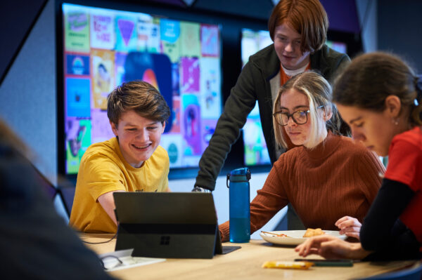 Three young people sat around a laptop, all engaged
