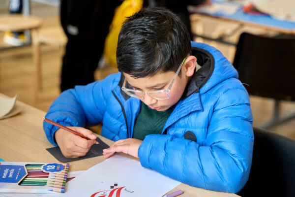 Young boy with glasses sat drawing calligraphy