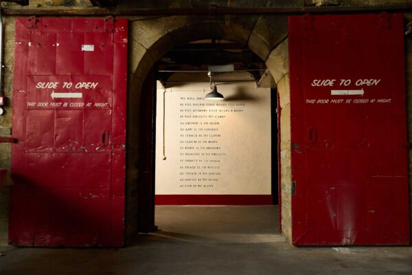 Red doors either side of an archway with a poem on the wall through the archway.
