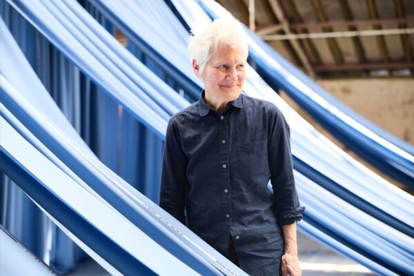 Artist Ann Hamilton stands among the blue material that makes up the giant curtain in We Will Sing