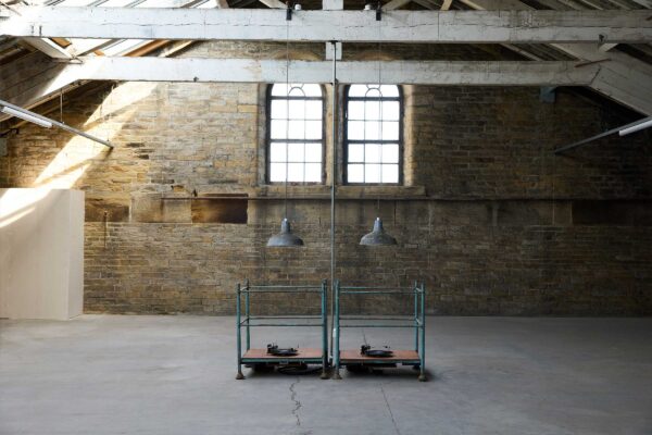 Two record players on metal stands with lampshades above them in the roof space of mill