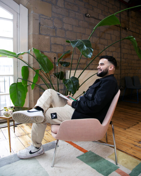 Tahir Shah sat on a pink chair with a large plant behind him.