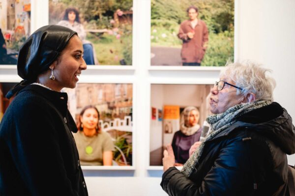 A younger and older lady chat to each other in front of a photo gallery