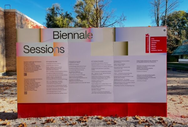 A very large outdoor sign which has 'Biennale Sessions' and lots of small text printed on it.