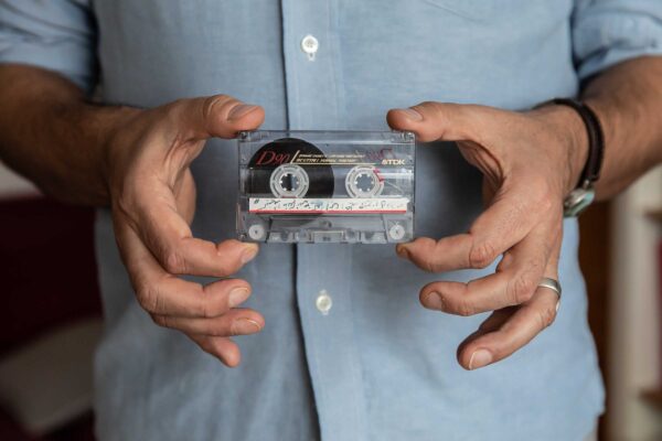 A man holds a plastic cassette tape.