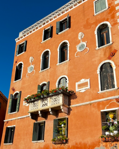 A bright orange coloured building with window boxes filled with plants and flowers in Italy.