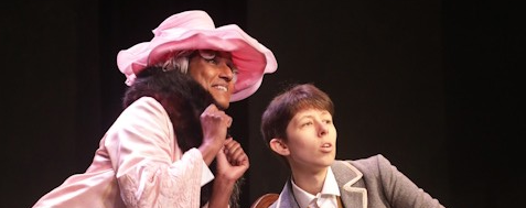 woman in pink and man in a suit sitting on a chair are looking up at the ceiling