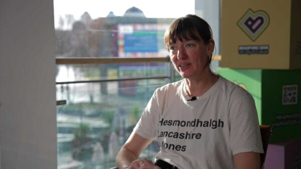 RISE Director Kirsty Housley wears a white t shirt in front of Bradford's City Square. She sits down for an interview.