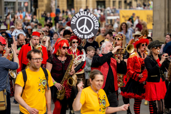 A crowd of people dance around a band, who are performing on the street.