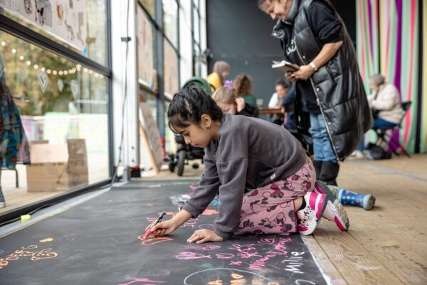 A young girl drawing on a black floor.