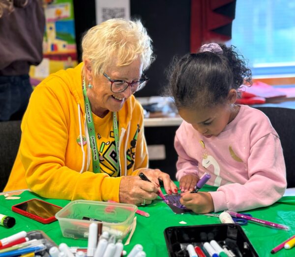 An older volunteer helping a young girl with her arts and crafts.