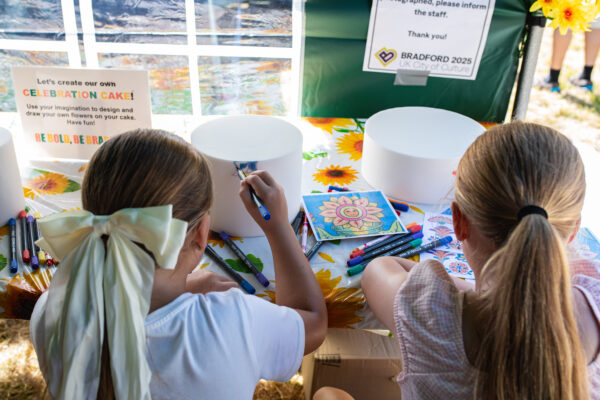 Two young girls drawing colourful patterns on a white cake