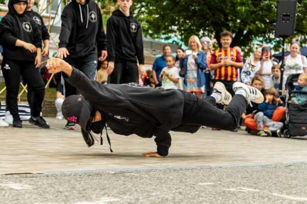 A break dancer balances on their hand in front of a crowd