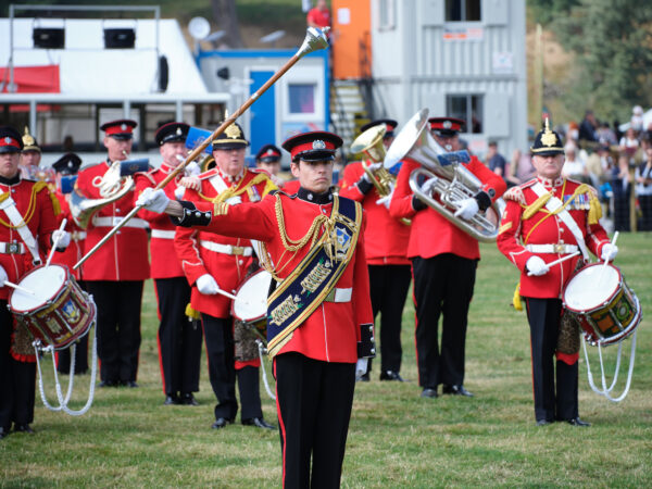 Smarty dressed men in red uniforms march with their instruments - led by a man with a long baton