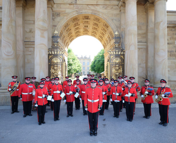 Smarty dressed men in red uniforms pose with their instruments in front of an arch