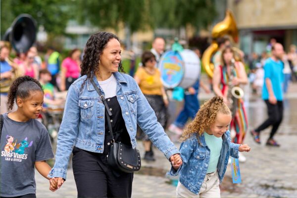 A woman and two children walk holding hands and smiling a band is playing in the background.