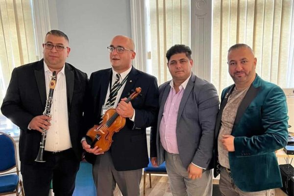 Four men in suits pose for a group picture. One is holding a clarinet, another is holding a violin