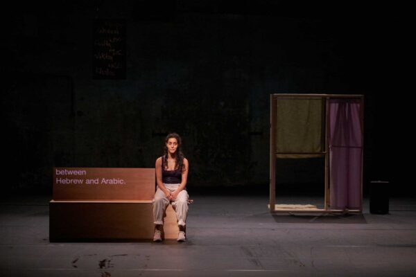 A performer sits on a stage, next to a box.