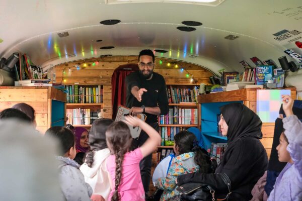 A man talks to a group of children in a bus which has been converted into a library