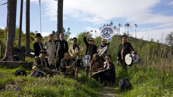 A group of musicians pose with their instruments on grass.