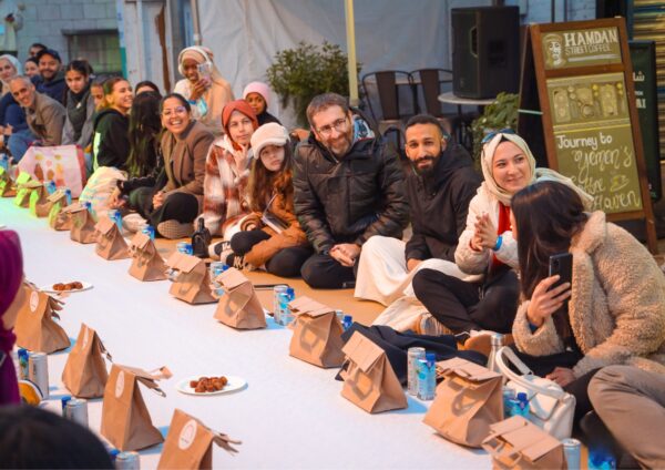 People sat on the floor, with brown paper bags in front of them. They are gathered to break their fast.