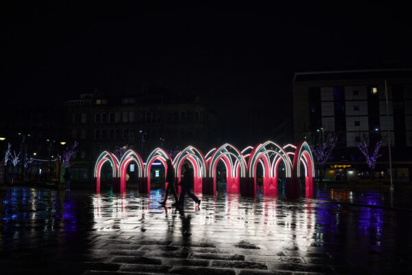 An Illuminated image of The Ramadan Pavilion, which is an arched structure that's positioned in Centenary Square. The floor is wet, so the lights are reflective on the floor.