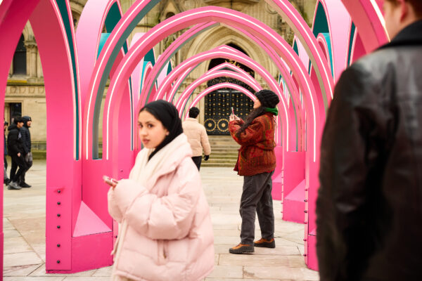 Three people interacting with the pink arched pavilion, named Infinite Light.