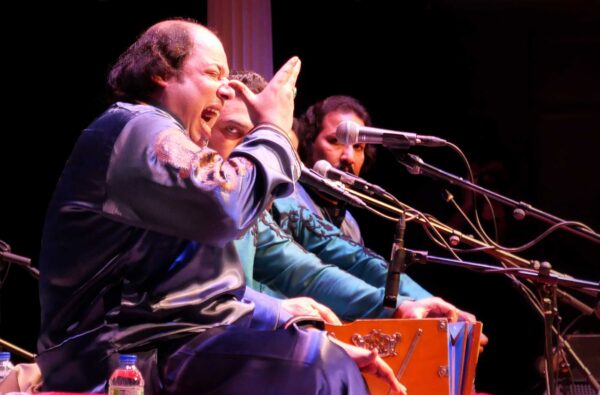 A performer singing into a microphone, with their hand raised.