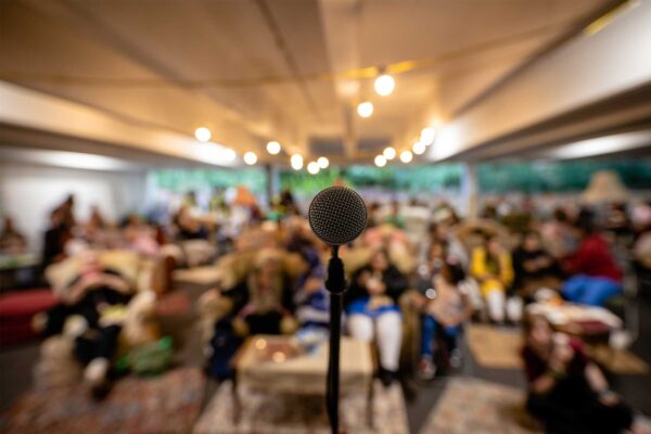 An image of a microphone in focus with a crowd of seated people blurred in the background