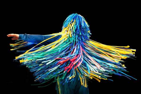 A parson spinning around with hundreds of pieces of colourful sticky tape hanging from their head