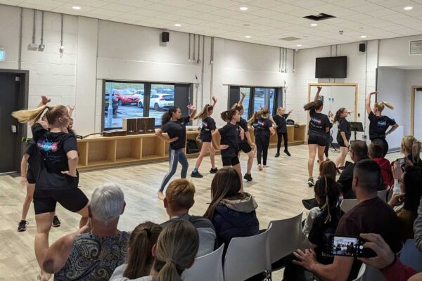 A group of girls dance in front of a crowd of people in a sports hall