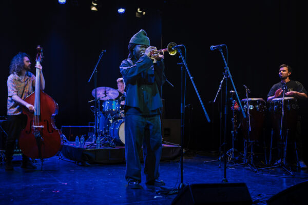 A black man plays the trumpet in front of a full band.
